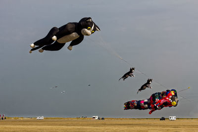 Low angle view of animal shaped kites flying above landscape against sky