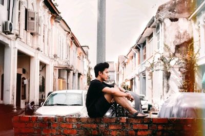 Side view of young man sitting on sidewalk in city