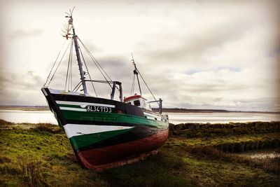 Boat moored on field by sea against sky
