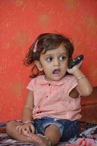 Portrait of cute girl sitting against red wall