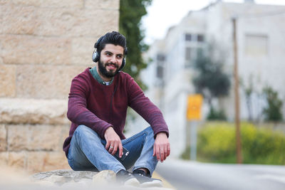 Young man sits on the wall, wearing a headphone