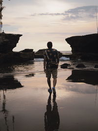 Man standing on rock at sea shore against sky