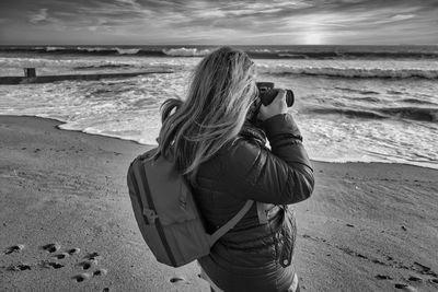 Rear view of woman photographing on beach