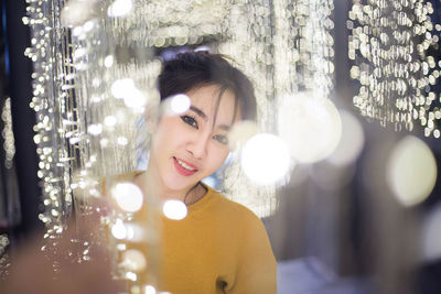 Portrait of smiling young woman amidst illuminated string lights