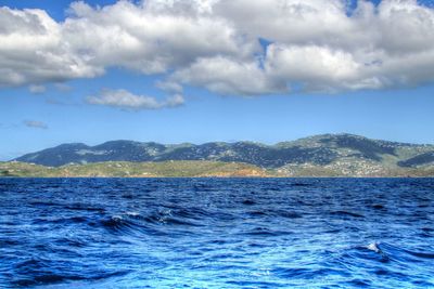 Scenic view of sea by mountain against sky