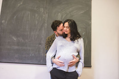 Man embracing pregnant girlfriend against blackboard at home