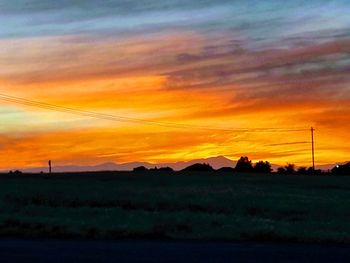 Scenic view of silhouette field against orange sky