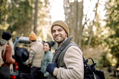 Side view of smiling man carrying backpack with friends in background