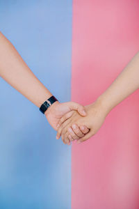 Close-up of hand of lovely couple holding together with pink background againts blue blackground