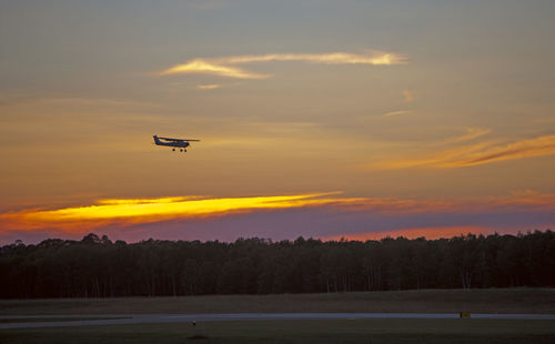 Silhouette airplane flying against sky during sunset