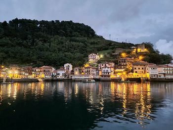 Illuminated buildings by lake against sky in town