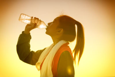 Woman drinking water against sky during sunset