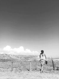 Shirtless man walking on land against sky during sunny day