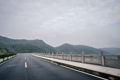 Road by mountains against cloudy sky