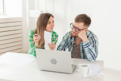 Man and woman using phone while sitting on table