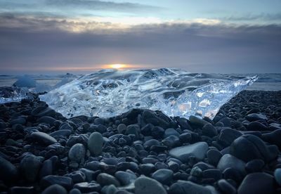 Close-up of pebbles at beach against sky during sunset