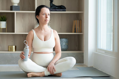 Pregnant woman holding bottle meditating at home