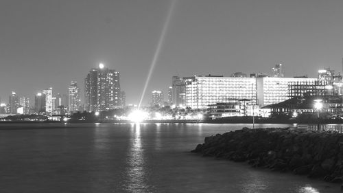 Illuminated buildings by sea against sky at night