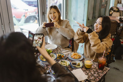 Happy female friends photographing food while sitting at restaurant