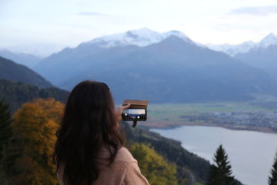 Rear view of woman photographing on mountain against sky