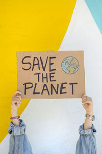 Unrecognizable cropped woman with save the planet banner standing against colorful wall during environmental event