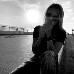 Young woman wearing sunglasses sitting against sky