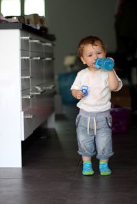 Portrait of boy drinking water from bottle while standing in kitchen