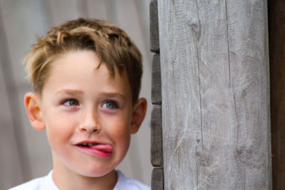 Close-up of cute boy sticking out tongue while standing by wooden wall