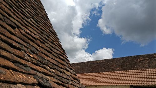 Low angle view of roofs against cloudy sky