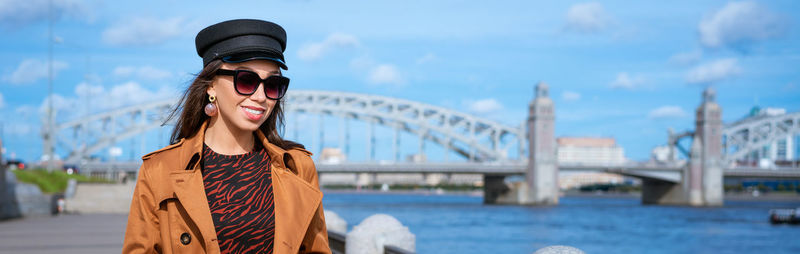 Happy young woman in light coat on the embankment posing