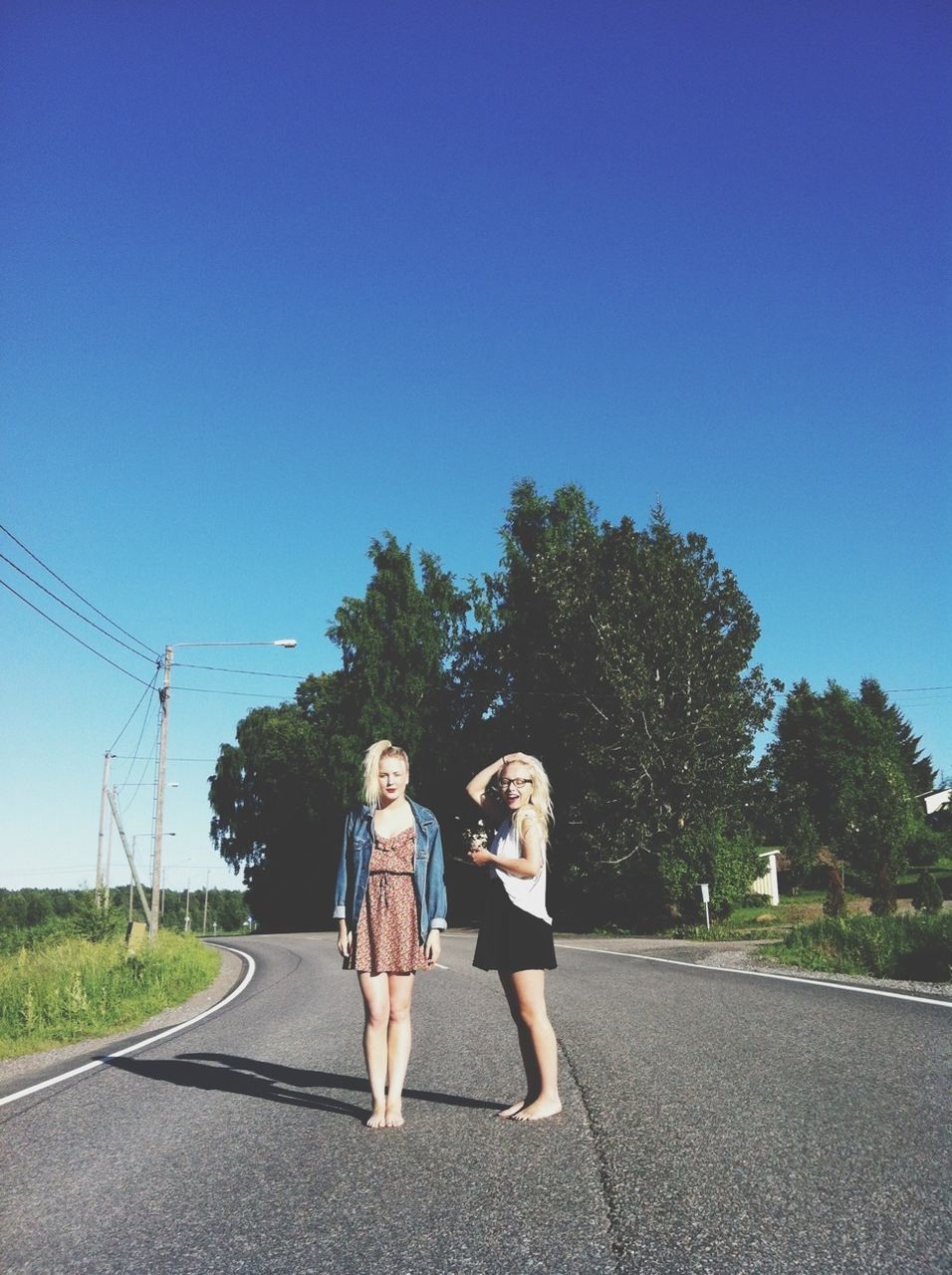 clear sky, road, full length, lifestyles, tree, leisure activity, transportation, street, rear view, blue, the way forward, copy space, casual clothing, standing, walking, sky, sunlight, day