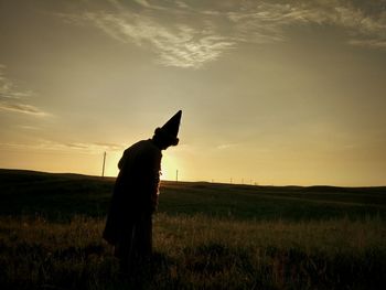 Silhouette man standing on field against sky during sunset