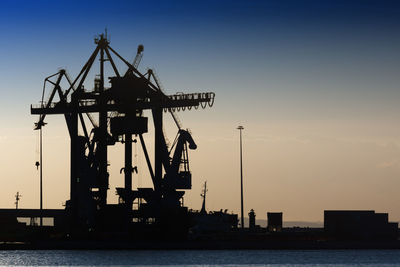 Silhouette cranes at commercial dock against sky during sunset in port ancona 