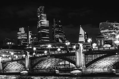 Illuminated bridge over river by buildings against sky at night