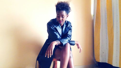 Beautiful young woman sitting against wall