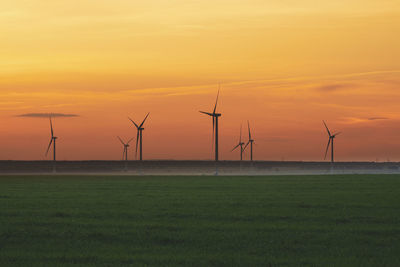 Windmills on field against sky during sunset