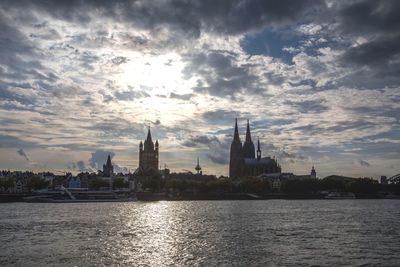 View of buildings by river against cloudy sky