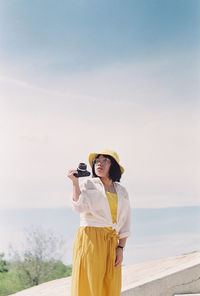 Rear view of woman photographing against sky during sunset