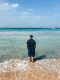 Rear view of man standing on beach against sky