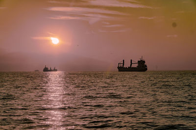 Silhouette boat sailing in sea against sky during sunset