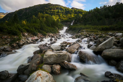 Stream flowing through rocks in river against sky