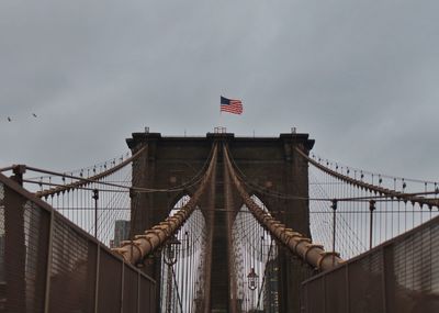 Low angle view of flags on bridge against cloudy sky