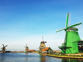 Traditional windmills by river against blue sky