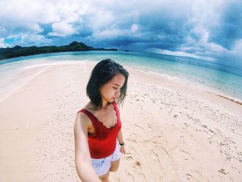 Young woman on sand at beach against sky