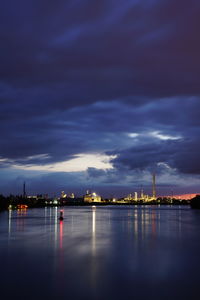 Illuminated city by sea against sky at night