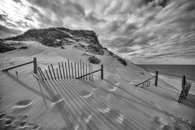 Sand dunes at beach against cloudy sky