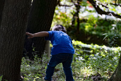 Rear view of man standing by tree trunk in forest