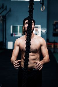 Shirtless man exercising with rope in gym