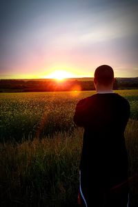 Rear view of silhouette woman standing on field against sky during sunset