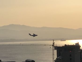 Airplane flying over sea against sky during sunset